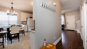 Una cocina moderna con armarios blancos, un comedor con mesa y sillas redondas, y un pasillo con un banco de madera y perchero.