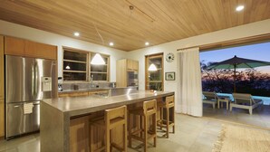 Cocina moderna con una isla central, taburetes de madera, electrodomésticos de acero inoxidable y vistas al exterior.