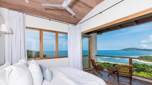 Un dormitorio con una cama grande, un ventilador de techo y un balcón con vista al océano.