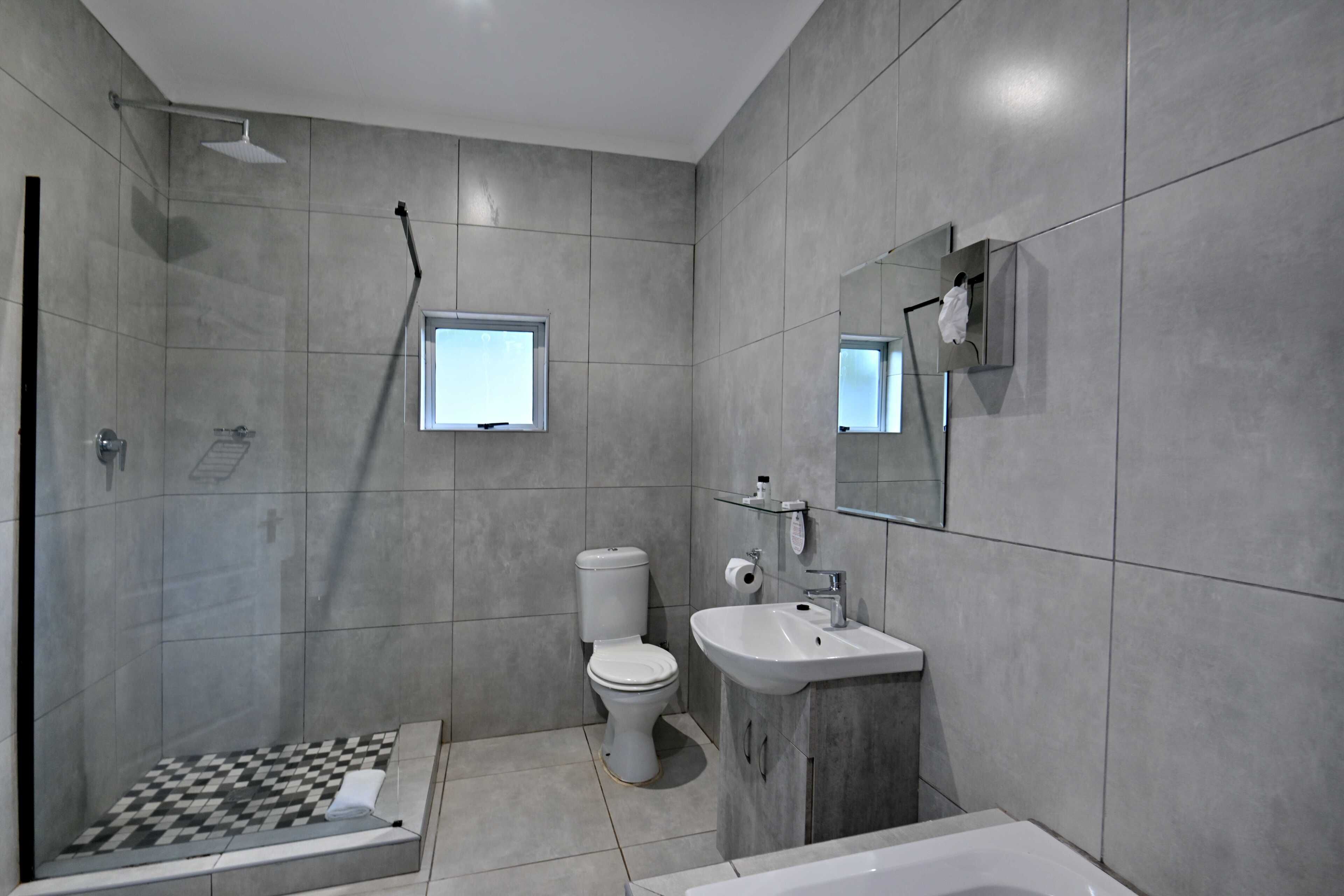 Un baño con ducha, inodoro, lavabo y una ventana pequeña.
