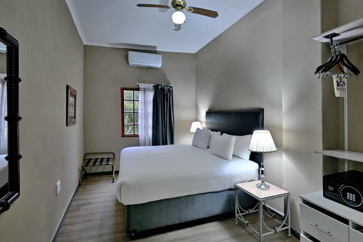 A hotel room with a bed, bedside table, lamp, and a ceiling fan.