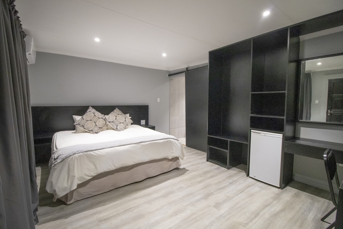 A modern bedroom with a bed, bedside tables, a built-in wardrobe, and a small white appliance.