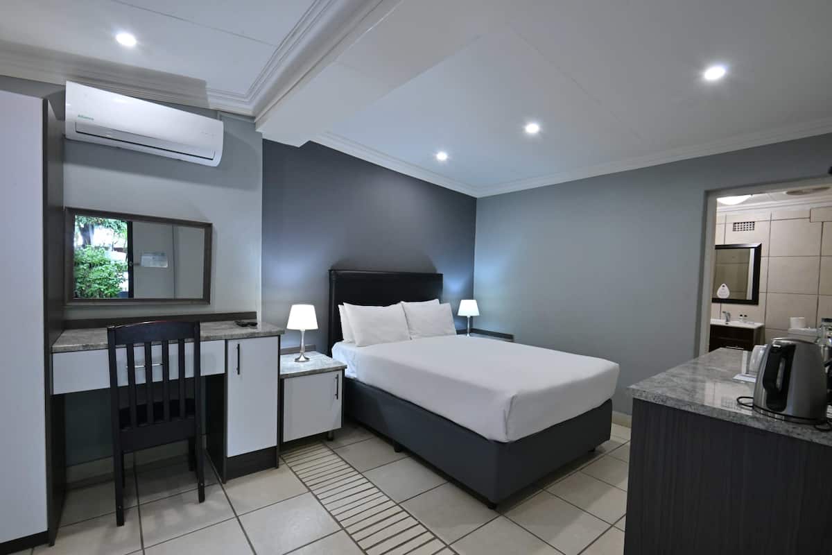 A hotel room with a bed, desk, chair, bedside lamps, and a coffee maker.