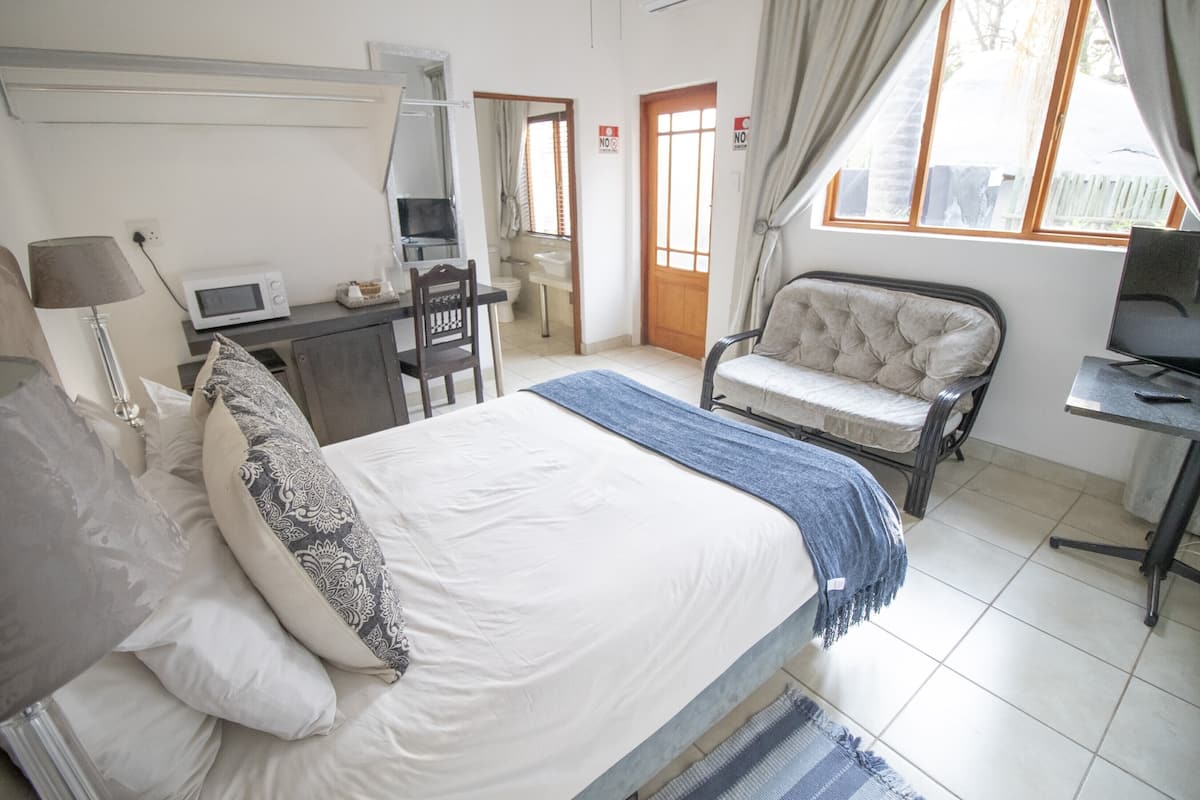 A bedroom with a bed, a desk, a chair, a TV, and a window.