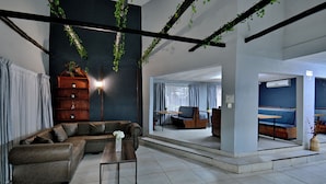 A modern interior with a sectional sofa, a coffee table, and a seating area with a view. - BON Hotel Rustenburg (Rustenburg)