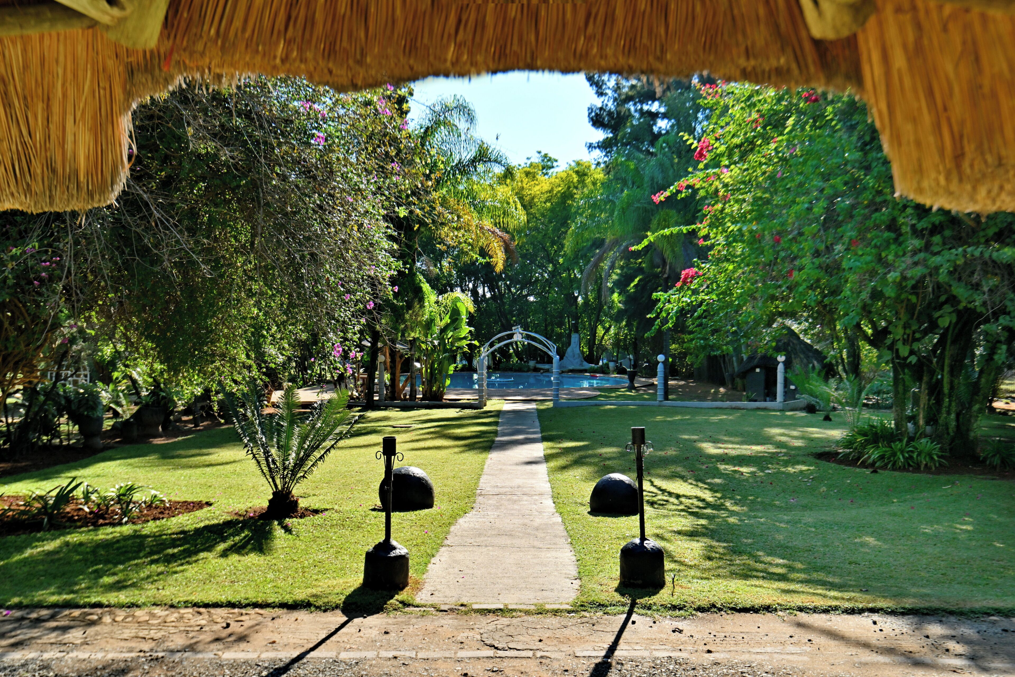 Un sentier qui traverse un jardin, avec une structure au toit de chaume qui le surplombe.