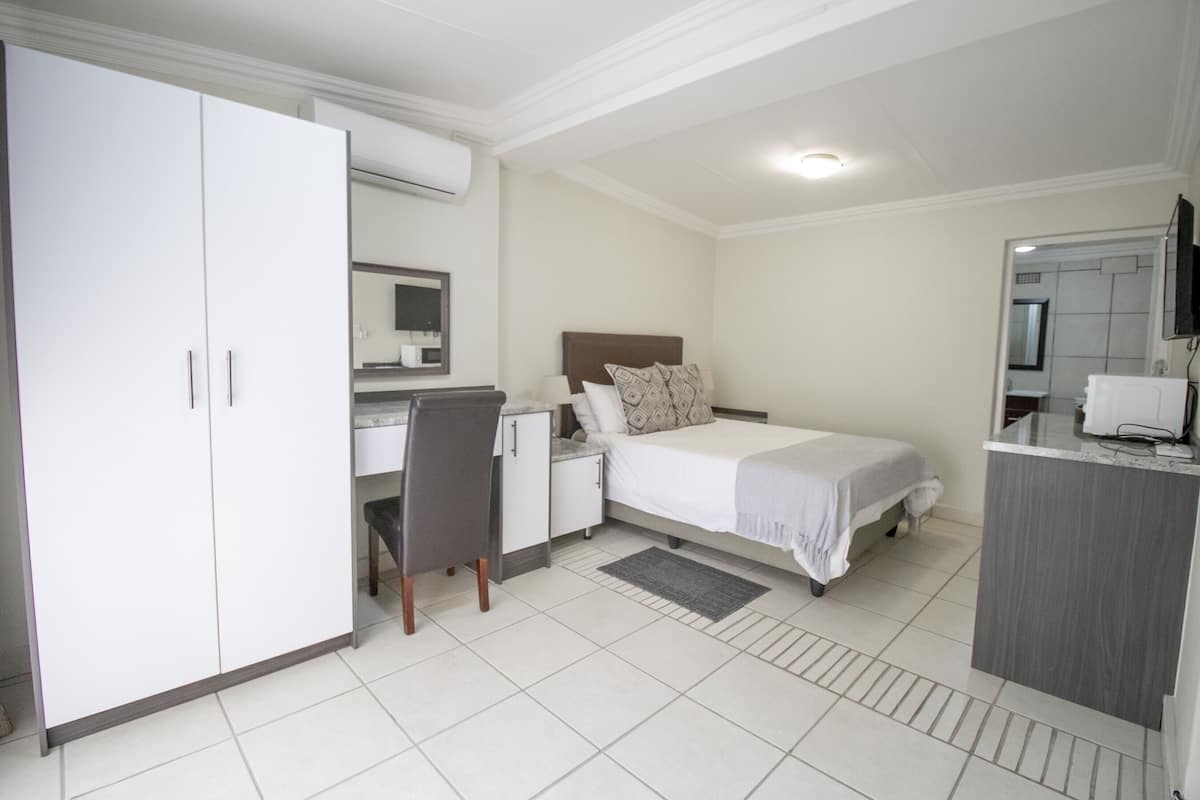 A bedroom with a bed, desk, chair, wardrobe, and a bathroom visible through an open door.