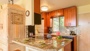 A kitchen with wooden cabinets, a granite countertop, a built-in oven, and a window with blinds. - Top Floor Ocean View & easy walk to the beach. Last minute booking 20 % discount (Kihei)
