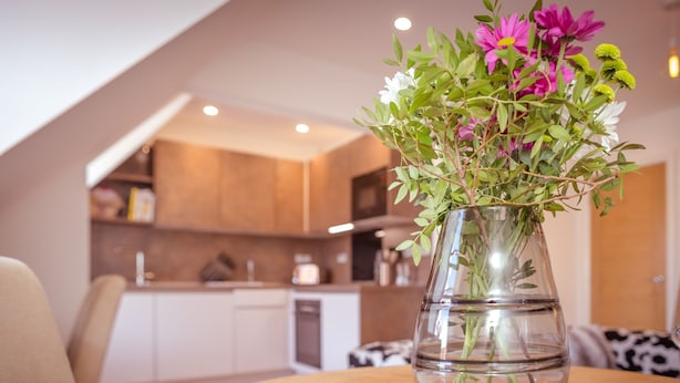 Ein Esstisch mit einer klaren Glasvase, in der Blumen stehen, einem weißen Teller und einer Küche im Hintergrund.