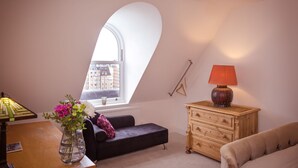 Ein gemütliches Schlafzimmer im Loft-Stil mit einem großen Fenster, einer Holzkommode, einem schwarzen Sofa und einem kleinen Tisch mit Blumen in einer Vase.