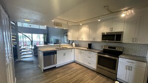 Une cuisine moderne avec des meubles blancs, des appareils électroménagers en acier inoxydable et un plancher en bois.