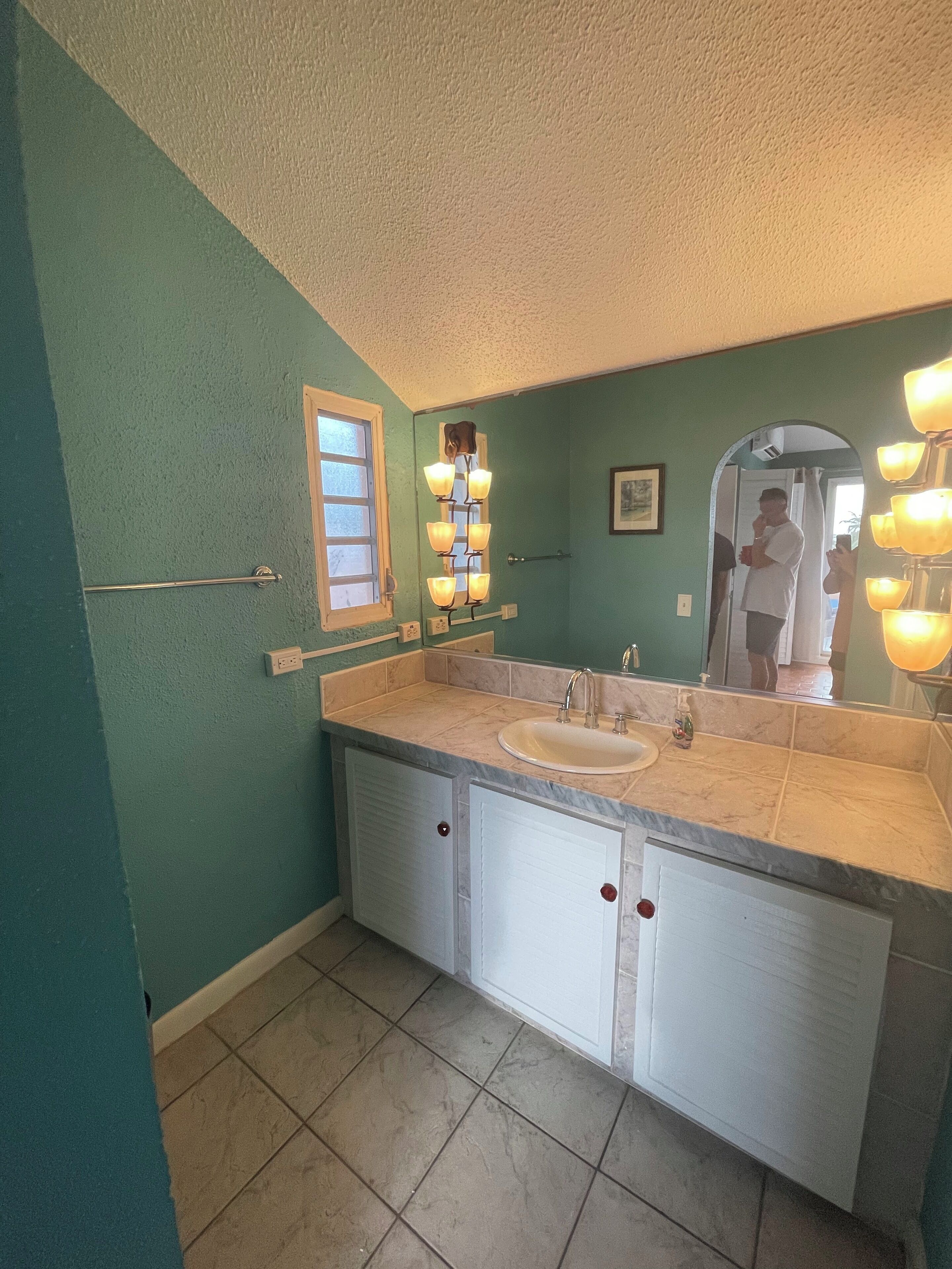 A bathroom with teal walls, a white vanity with a sink, and a mirror with lights.