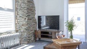 Ein modernes Wohnzimmer mit Steinwand, Flachbildfernseher, Holzmöbeln und einem Glas Wein auf einem Tablett.