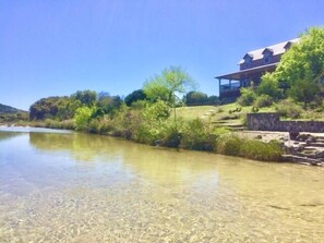 Ein Haus mit Blick auf den Fluss, umgeben von Grün und unter blauem Himmel.