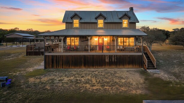 A two-story house with a covered porch and a deck, surrounded by a grassy area and trees. - 4 Maples on the Frio, Riverfront, Wi-Fi, @ Frio River Vacation Rentals (Concan)