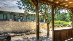 Un espace extérieur abrité, doté d’un mur en pierre, d’un barbecue et d’un banc en bois.