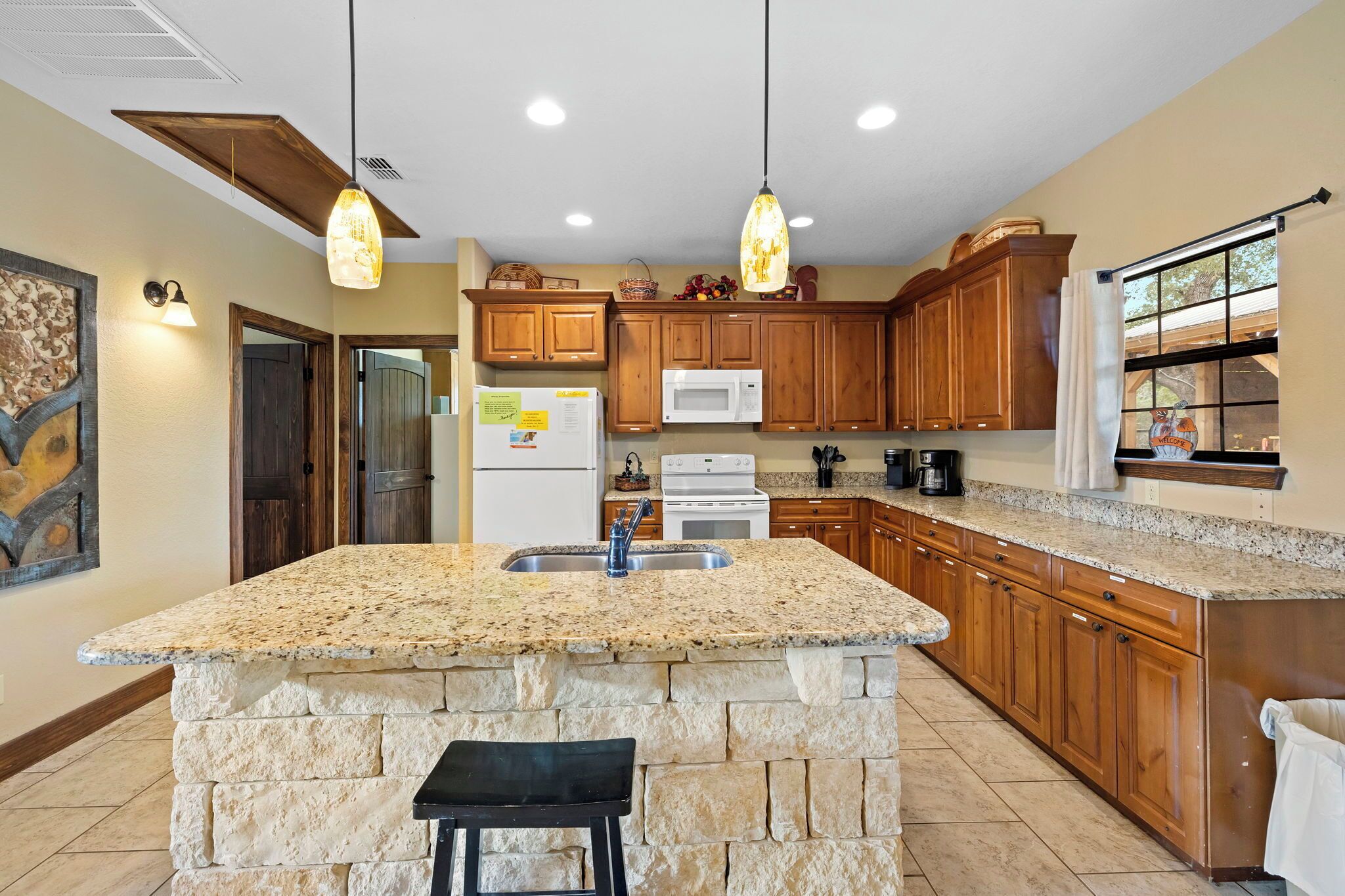 A kitchen with granite countertops, wooden cabinets, a stone island, and pendant lighting.