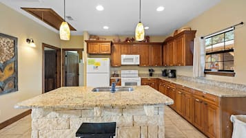 A kitchen with granite countertops, wooden cabinets, a stone island, and pendant lighting.