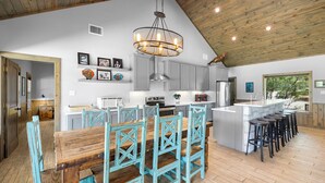 A spacious kitchen with a wooden dining table, teal chairs, and a central island with bar stools. - Celebration Station, Private Pool, Wi-Fi, @ Frio River Vacation Rentals (Concan)