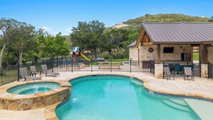 A swimming pool with a stone border, a children's play area, and a barbecue area with outdoor seating. - Celebration Station, Private Pool, Wi-Fi, @ Frio River Vacation Rentals (Concan)