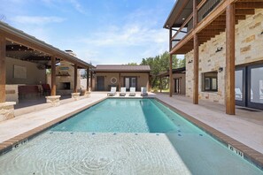 A swimming pool with lounge chairs and a stone building in the background. - FrioRitas Private Pool, Wi-Fi, @ Frio River Vacation Rentals (Concan)