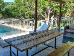 A covered outdoor area with a pool, wooden benches, and lounge chairs.