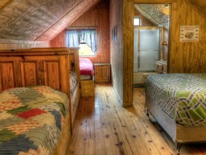 A cozy attic bedroom with two beds, wooden walls, a small window, and a refrigerator.