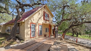 A rustic cabin with a stone foundation, wooden deck, and a red roof. - Stonehaven @ Frio River Vacation Rentals (Concan)