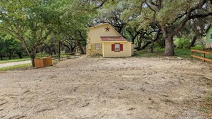 A small yellow building with a red roof and a red star emblem, surrounded by large trees and a gravel path. - Stonehaven @ Frio River Vacation Rentals (Concan)