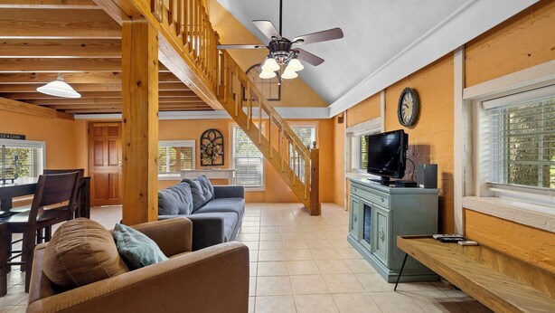 A spacious living area with a wooden staircase, a sofa, a television, and a dining area. - Stonehaven @ Frio River Vacation Rentals (Concan)