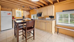 A kitchen with wooden beams, a dining table with chairs, a refrigerator, a stove, and a microwave. - Stonehaven @ Frio River Vacation Rentals (Concan)