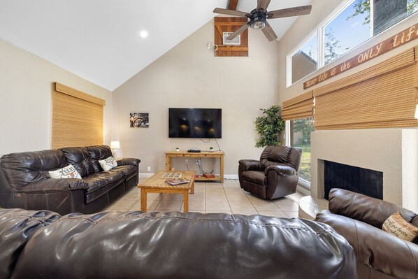 A spacious living room with leather sofas, a wooden coffee table, a flat-screen TV, and a fireplace.