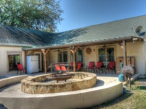 An outdoor patio with a stone fire pit, red chairs, and a barbecue grill.