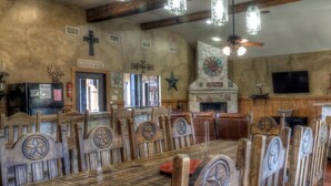A rustic dining area with wooden tables and chairs, a fireplace, and a television. - Rustic Tavern @ Frio River Vacation Rentals (Concan)