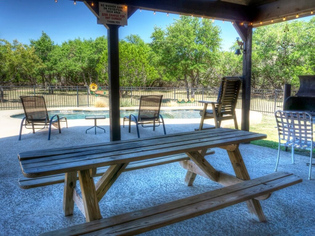 En udendørs terrasse med picnicborde og stole, grill og swimmingpool.