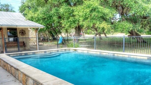 A rectangular swimming pool with a stone border, surrounded by a metal fence, and a building with a sign indicating it is closed.