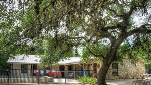 A building with a stone exterior, a covered patio area, and a fenced outdoor space with a tree providing shade.