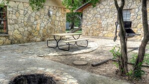 A stone patio with a fire pit, picnic table, and barbecue grill.