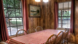A dining area with a checkered tablecloth, wooden chairs, and a painting on the wall.