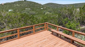 A wooden deck with a railing overlooking a hilly landscape with sparse vegetation and a clear sky. - Coyote Canyon Lodge, Private Pool, @ Frio River Vacation Rentals (Concan)