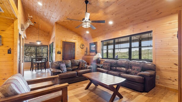 A cozy cabin interior with a wooden ceiling, a ceiling fan, a leather sofa, a wooden coffee table, and a dining area with a table and chairs. - Coyote Canyon Lodge, Private Pool, @ Frio River Vacation Rentals (Concan)