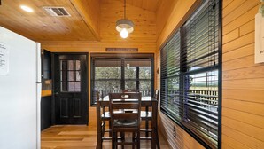 A wooden interior with a dining table and chairs, a black door, and a window with blinds. - Coyote Canyon Lodge, Private Pool, @ Frio River Vacation Rentals (Concan)