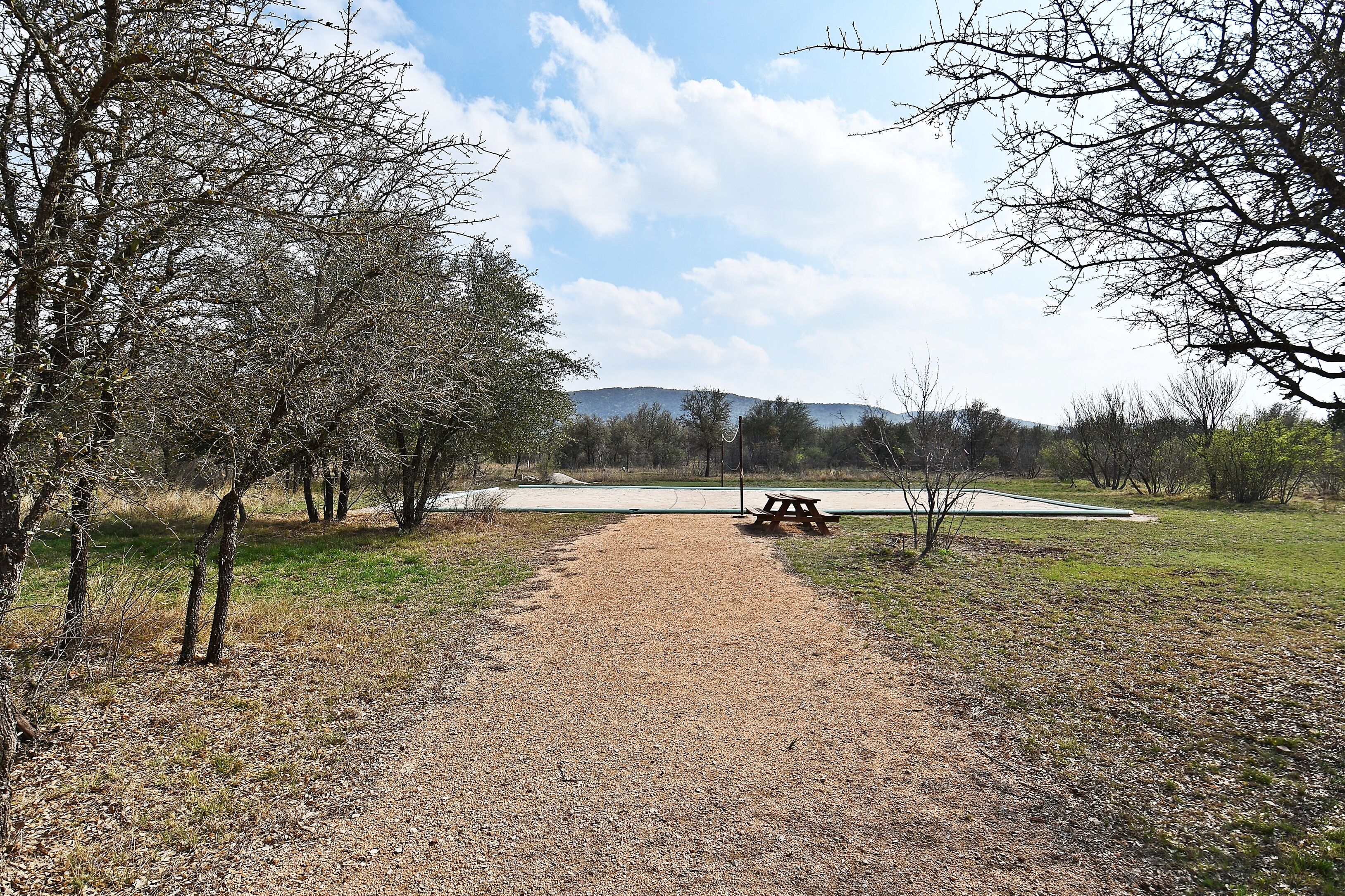 A gravel path leading to a picnic area with a bench, surrounded by trees and a view of distant hills.