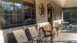 A covered outdoor seating area with wooden benches and chairs, a stone wall, and a large window overlooking a garden. - Deer Trail @ Frio River Vacation Rentals (Concan)