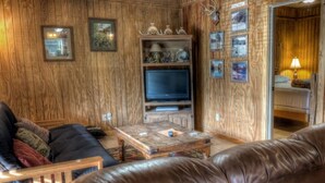A cozy living room with a leather couch, wooden coffee table, and a television. - Deer Trail @ Frio River Vacation Rentals (Concan)