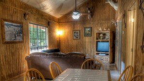 A wooden interior with a sofa, dining table, chairs, and a television. - Deer Trail @ Frio River Vacation Rentals (Concan)