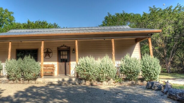 A building with a covered porch, wooden columns, and a star-shaped decoration. - Deer Trail @ Frio River Vacation Rentals (Concan)