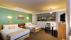 A hotel room with two beds, a desk with a chair, a TV, and a window with a city view. - Hotel Estoril (Mexico City)