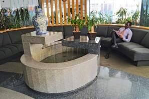 Un vestíbulo con zona de estar, una fuente decorativa y plantas en macetas.