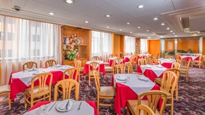 A banquet hall with multiple tables set for dining, wooden chairs, and a carpeted floor. - Hotel Estoril (Mexico City)